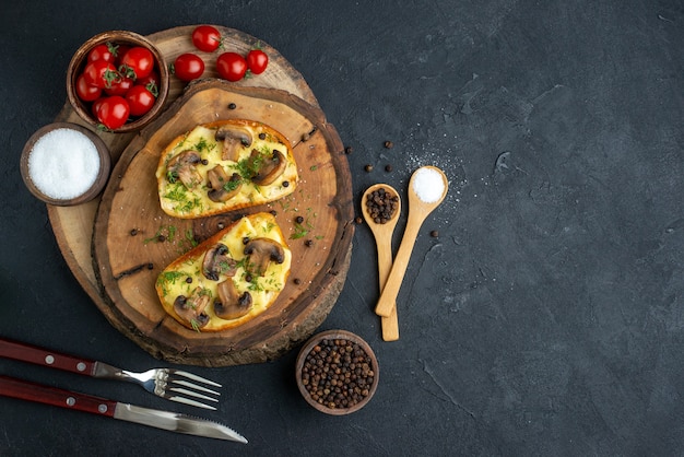 Overhead view of tasty snack with mushrooms tomatoes salt on wooden board cutlery set on black background