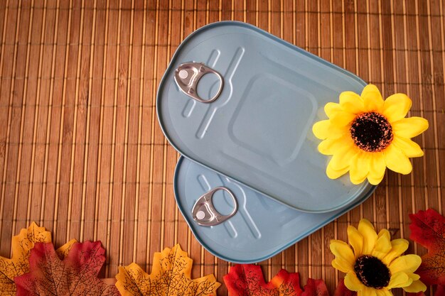 overhead view of tin cans with a yellow flower and maple leaves on bamboo tablecloth