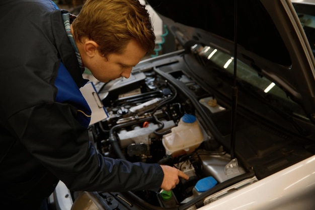 Overhead view of a young professional auto mechanic inspecting the car under hood, examining the engine in a car repair workshop . Close-up