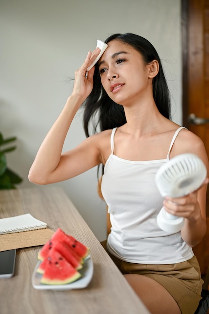 An overheated Asian woman wiping her sweat on her face and cooling herself down