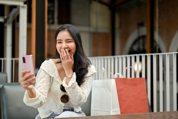 Overjoyed Asian woman video call with her friend while relaxing in the mall relaxation area