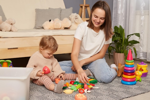 Overjoyed loving young Caucasian mother play with toys plastic fruit with small baby daughter Happy smiling mom have fun feel playful with little toddler kid child Parenthood