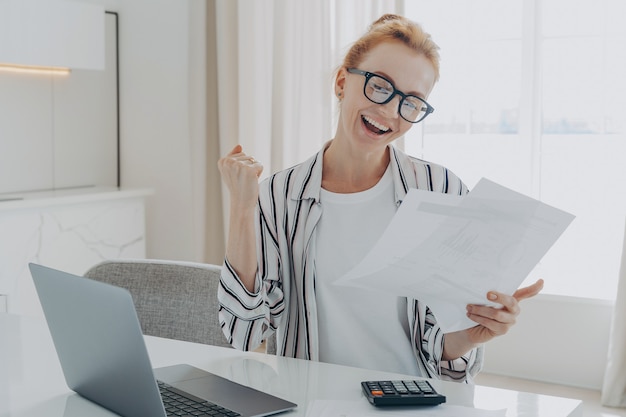 Overjoyed redhead woman exclaiming yes celebrating money refund or last last mortgage payment