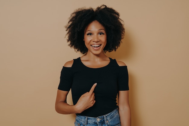 Overjoyed young mixed race woman pointing finger at herself and looking at camera with amazed face expression