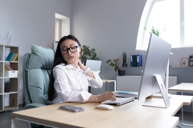 Overtired asian woman office worker has severe neck pain massages neck muscles with hand female