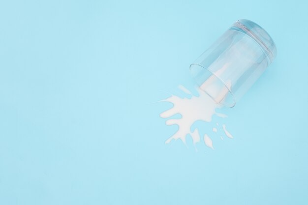 Overturned glass with milk on blue background