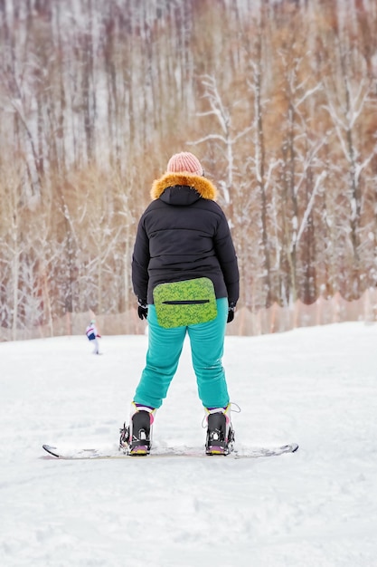 An overweight girl learns to snowboard from  mountainside view from the back winter holiday at ski resort