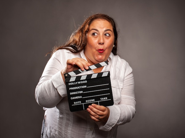 Overweight woman holding a movie clapper board on a grey background