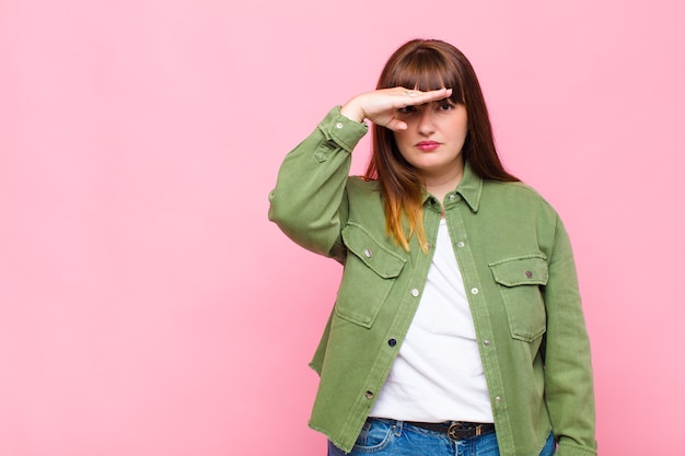 Overweight woman looking bewildered and astonished, with hand over forehead looking far away, watching or searching