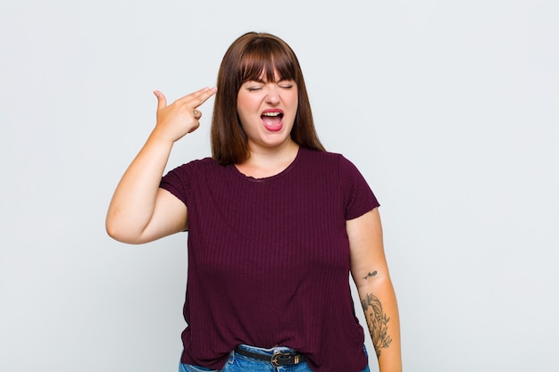 Overweight woman looking unhappy and stressed, suicide gesture making gun sign with hand, pointing to head