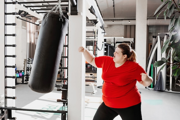 overweight woman in sportswear is boxing punching bag in the gym