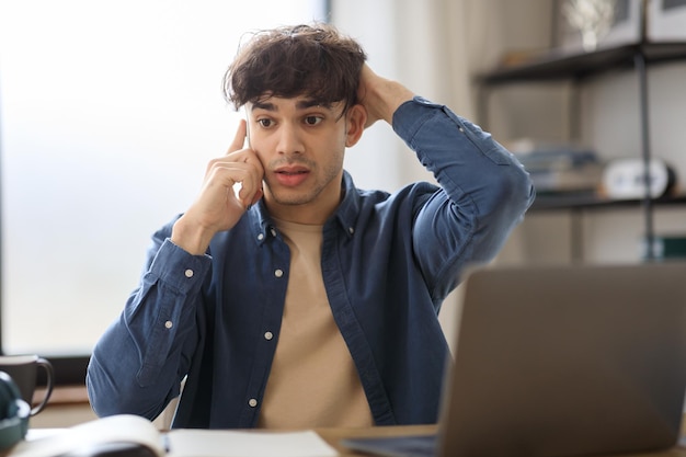 Overwhelmed manager man talking on phone at workplace near laptop