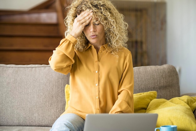 Overwork and stress bad health condition Adult woman touching his front and head with pain Tired and worried female people using laptop computer at home sitting ont he sofa Stock market fall down