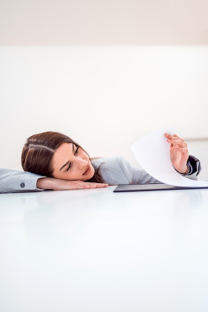 Overworked business woman lying at the desk and looking at paperwork, copy space.