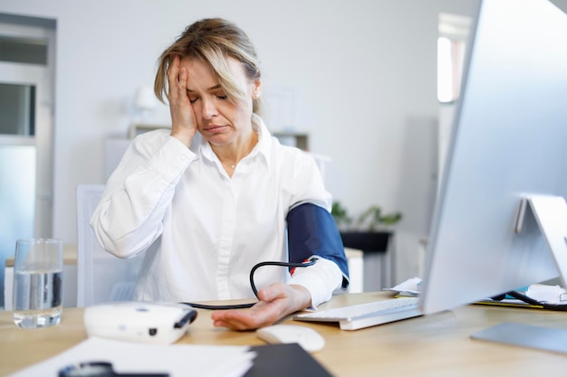 Overworked business woman measuring arterial pressure with a blood pressure monitor