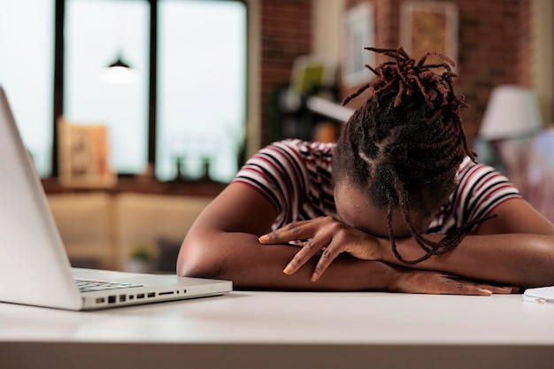 Overworked freelancer sleeping on table at daytime, sleepy stressed remote worker, professional burnout. Tired student lying on desk, exhausted african american employee having break at workplace