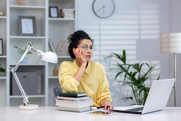 Overworked and overwhelmed woman studying remotely hispanic woman upset sitting at desk inside home