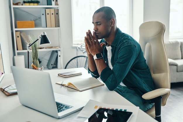 Overworked. Tired young African man in shirt keeping eyes closed while sitting in the office