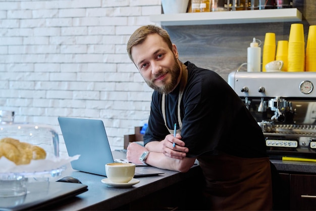 Photo owner coffee shop worker young male with laptop on the counter