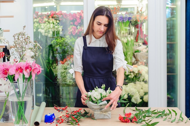 The owner of a flower shop makes a bouquet with white roses