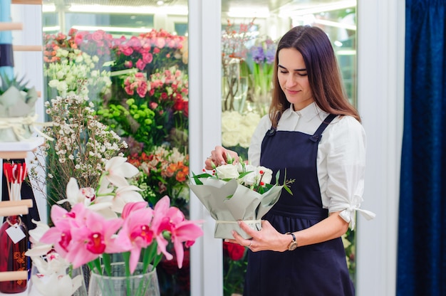 The owner of a flower shop makes a bouquet with white roses