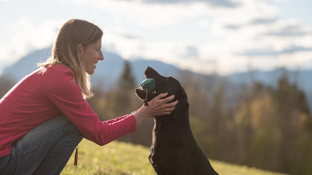 Owner lovingly praising her black labrador retriever holding a dummy