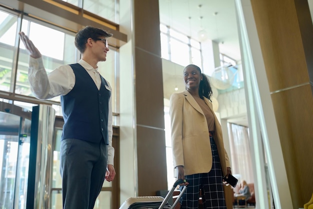 Owner of receptionist of hotel in uniform meeting black woman with suitcase