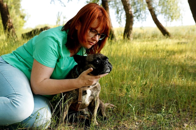 Owner talking to her dog french bulldog in the park on a summer day sitting on the grass