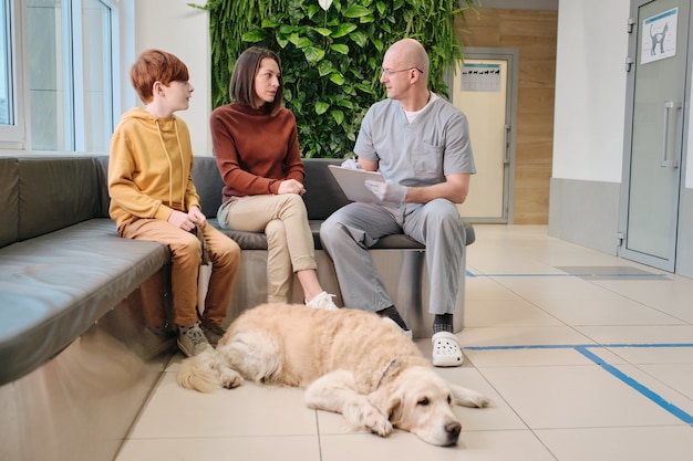 Owners of labrador consulting with veterinarian who making notes in medical card at clinic