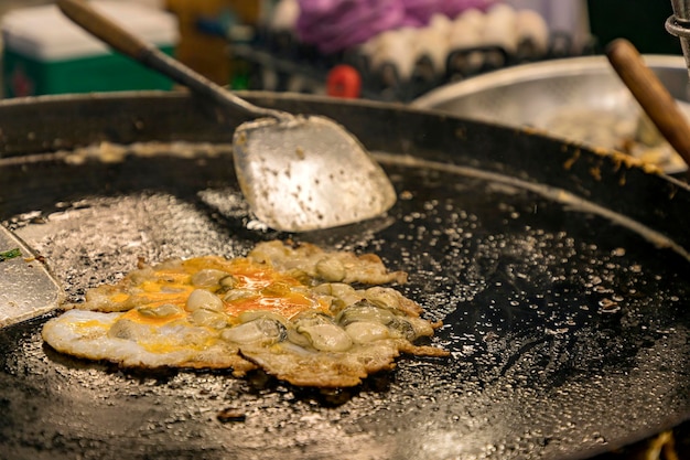 Oysters fried while on a hot black pan Asian style circle and spatula a delicious Thai dish made with oysters flour eggs and fried until crispy famous thai food called HoyTod Selective focus