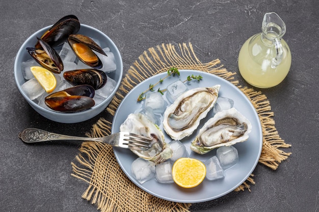 Oysters ice lemon and fork on plate Clams in shells in bowl Bottle with lemon juice Flat lay Black background