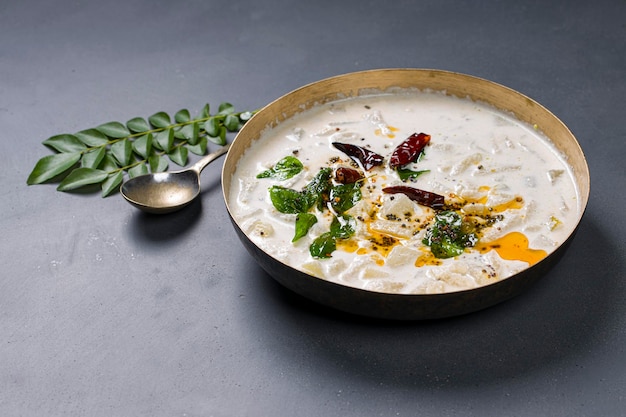 Pachadi or Raithasouth Indian side dish made using ash guard curd and coconut placed in a brass vessel  with grey background