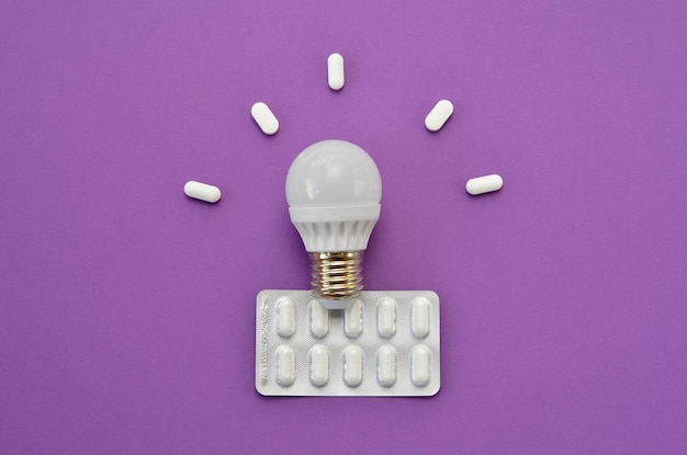 Pack of pills and light bulb on purple background