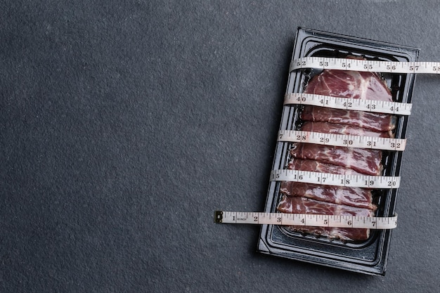 Pack of raw sliced Dry Aged beef in black plastic tray and waist tape on black stone table background Food and healthcare concept