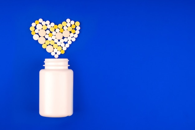 Pack with a heap of medical multicolored pills in the form of a heart on a blue background