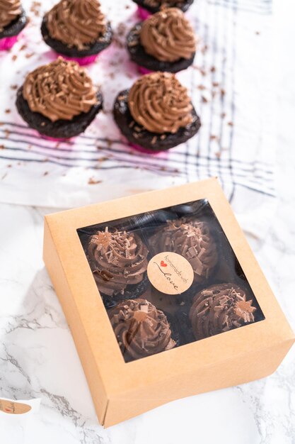 Packaging chocolate cupcakes with chocolate ganache frosting into a paper cupcake box.