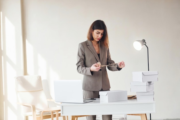 Packaging orders into the white boxes Young woman in formal clothes is indoors Conception of style