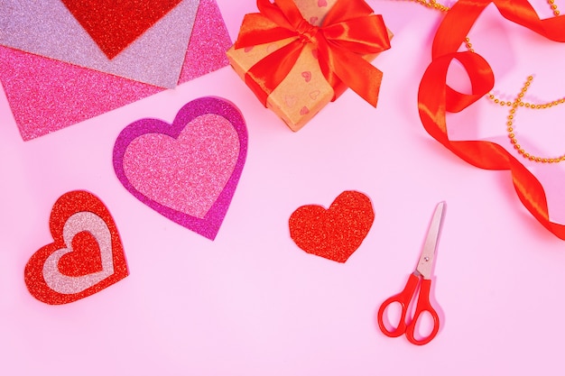 Packaging Valentine's Day or birthday presents. Valentine's Day gifts with a red paper heart on a pink surface. Top view. Tools for handicraft paper hearts.