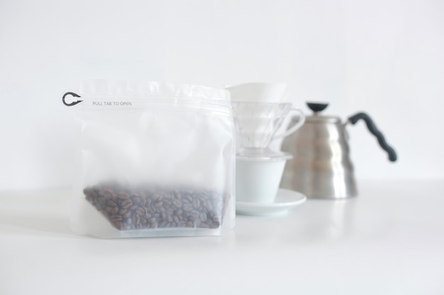 Packed coffee beans arranged with set coffee maker on white background