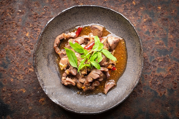 Pad Ka Prao Kruang Nai Gai, Thai food, basil stir fried chicken offal, variety meats, pluck or organ meats in wabi sabi style plate on rusty texture background, top view