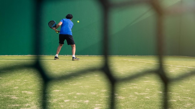 Padel player with black racket playing a match in the open behind the net court