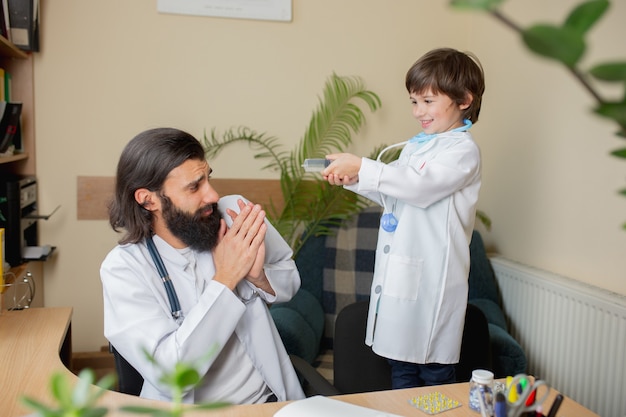 Photo paediatrician doctor examining a child in comfortabe medical office. healthcare, childhood, medicine, protection and prevention concept. little boy trust to doctor. having fun while taking medicine