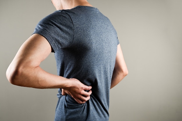 Pain in back and kidneys of man. A man in a T-shirt holds his hand on his lower back.