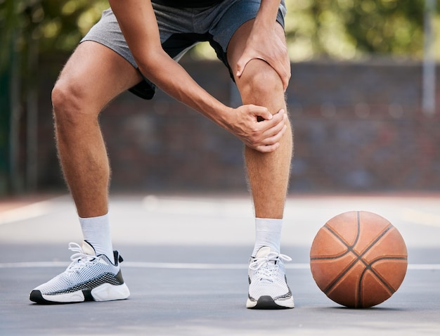 Pain basketball and man with knee injury standing on outdoor court holding leg Sports fitness and athlete with joint pain injured and hurt in training workout and game on basketball court