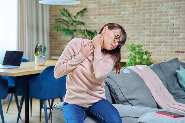 Photo pain in neck disturbing middleaged woman suffering female sitting at home