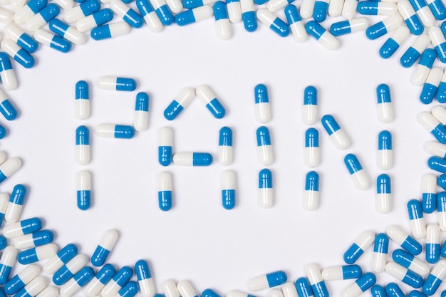 Pain word text made of blue tablets pills and capsules on white background