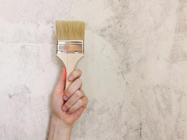 Paint brush in hand. Beige background. Repair in the apartment. Place for text.