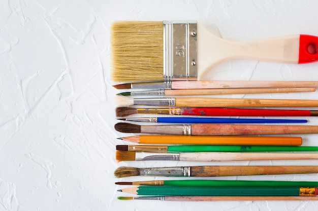 Paint brushes of different sizes and pencils on white texture background Art and education object