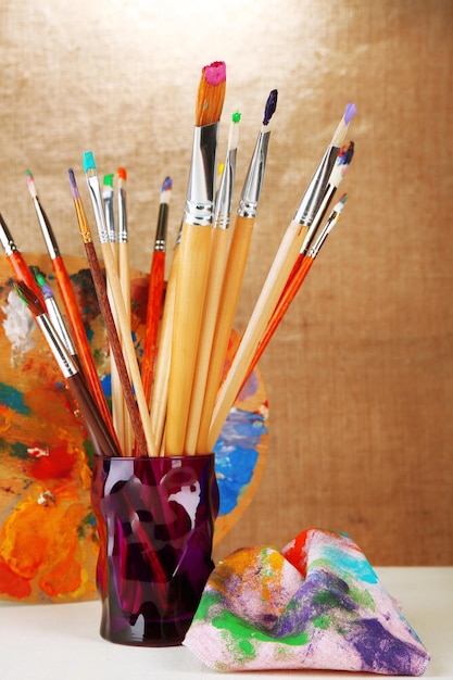 Paint brushes with paints and palette on beige background