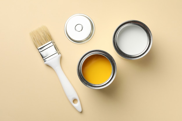 Paint cans and brush on beige background, top view